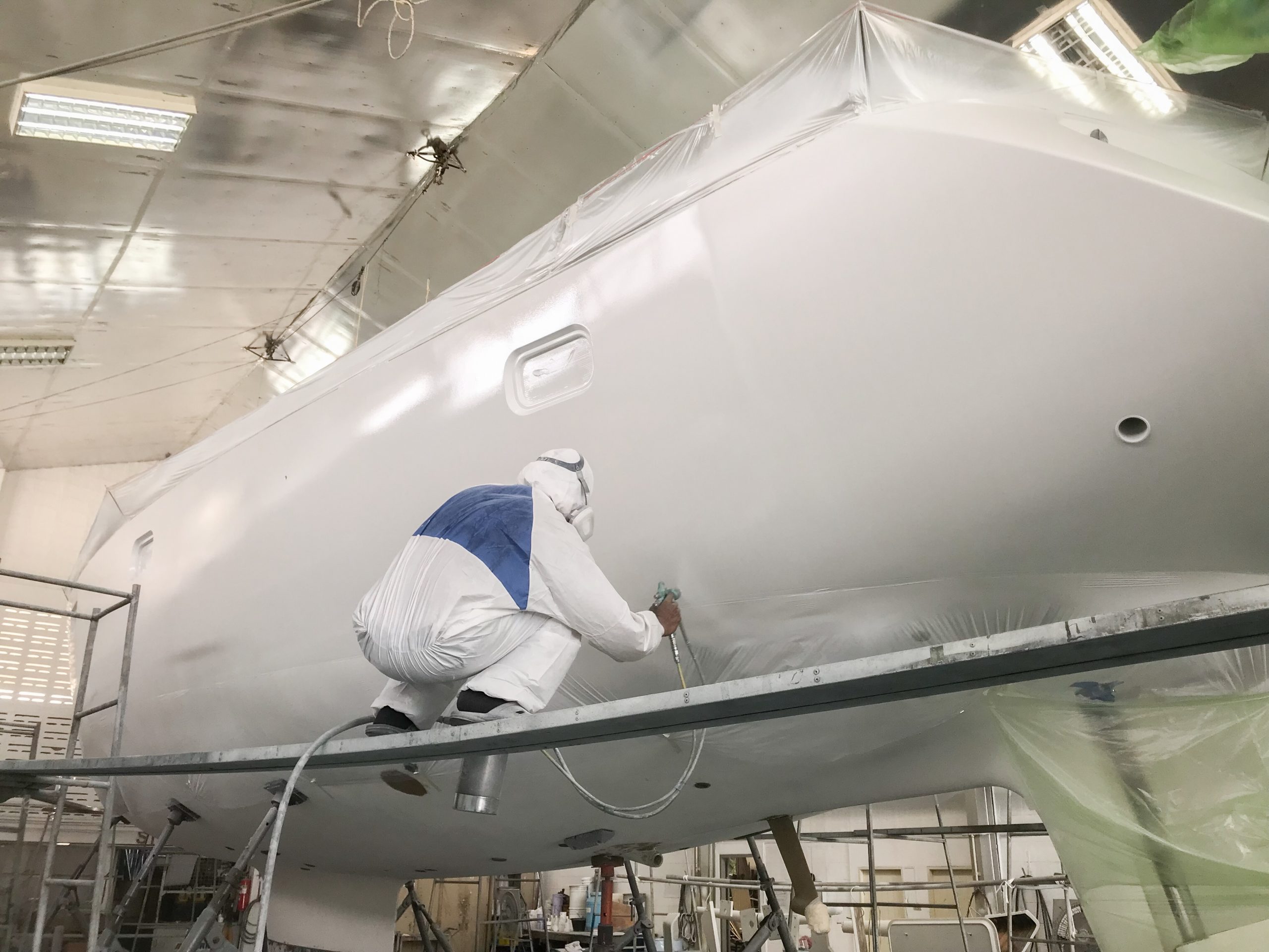 Man spraying white paint on the under part of a boat.